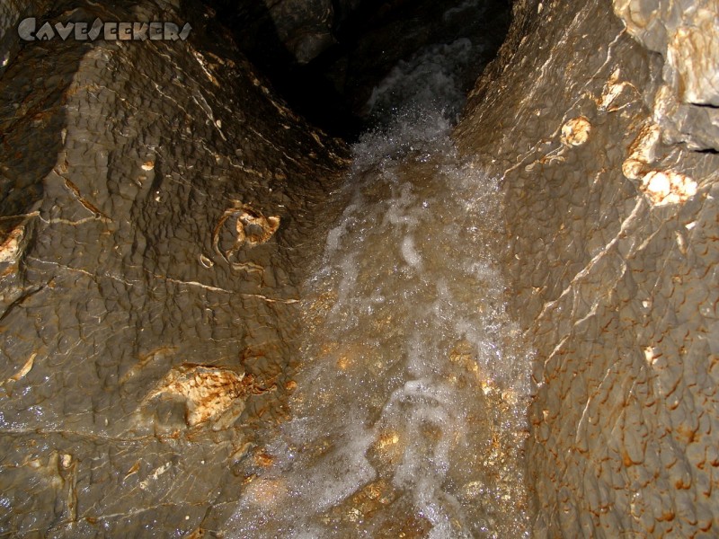 Brunneckerhöhle: Kleiner Wasserfall vor in grauem Material eingebackenem weißen Material.